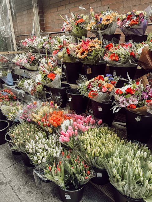 A display of numerous floral arrangements and bouquets in a flower shop, showcasing a variety of fresh flowers including pink and white tulips, orange tulips, and mixed seasonal blooms with vibrant co